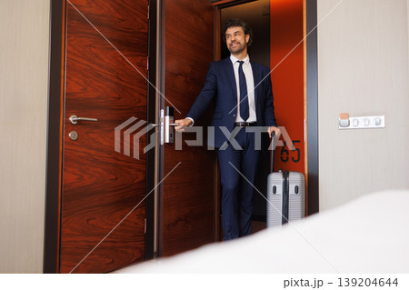 Smiling Business Traveler Opening Hotel Room Door With Suitcase After Check In 139204644