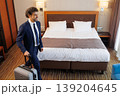 Businessman arriving to hotel room with suitcase and looking at comfortable bed 139204645