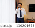 Smiling Businessman Talking on Phone While Adjusting Tie in Hotel Room 139204653