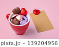 Valentine's Day concept with heart chocolates in red coffee cup and blank brown craft paper card on pink background 139204956