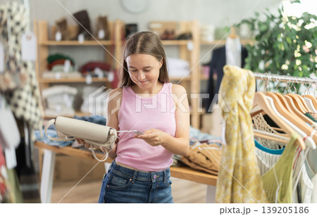 Young teen girl shopping - choosing a fashionable handbag in clothing store 139205186
