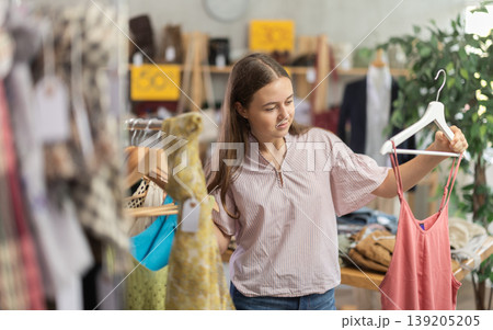 Positive teenage girl choosing something for summer in clothing store 139205205