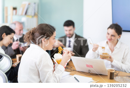 Group of colleagues, man and woman, are having lunch in office during their break, eating noodles Group of colleagues, man and woman, are having lunch in office during their break, eating noodles 139205232