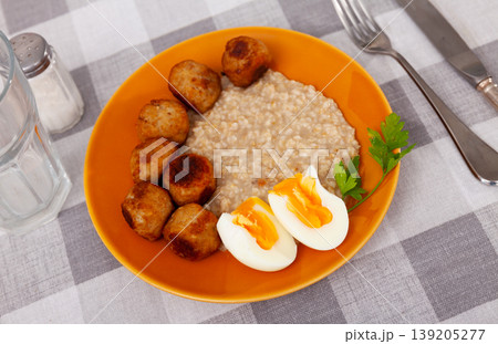 Soft-boiled eggs, golden meatballs and oatmeal on orange plate Soft-boiled eggs, golden meatballs and oatmeal on orange plate 139205277