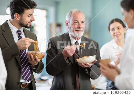 Group of colleagues, man and woman, are having lunch in office during their break, eating noodles Group of colleagues, man and woman, are having lunch in office during their break, eating noodles 139205420