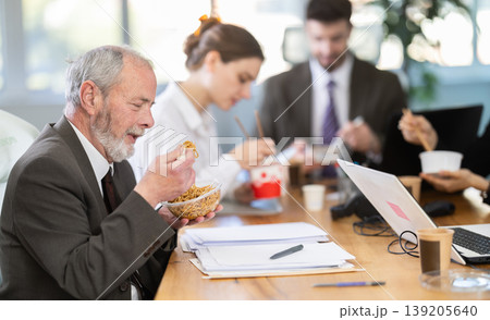 Lunch break - mature man eating noodles with colleagues in modern office 139205640