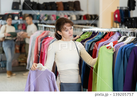 Woman buyer in store has removed hanger with blouse from window and is considering product. 139205757