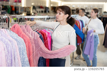 Woman stopped near leisure wear showcase, holds eiderdown bathrobe hanger in hands, examines product Woman stopped near leisure wear showcase, holds eiderdown bathrobe hanger in hands, examines product 139205765