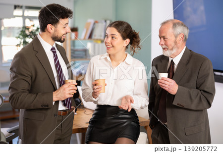 Young woman and two man co-worker drinking coffee and friendly talking during break while working in office Young woman and two man co-worker drinking coffee and friendly talking during break while working in office 139205772