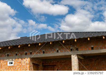 Roof installation takes place on a building with a metal tile roof, showcasing an ongoing construction process and blue sky above 139205797
