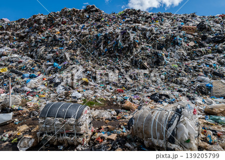 A large heap of waste is present at a municipal garbage dump with trash bags and plastic scattered across the ground during daylight A large heap of waste is present at a municipal garbage dump with trash bags and plastic scattered across the ground during daylight 139205799