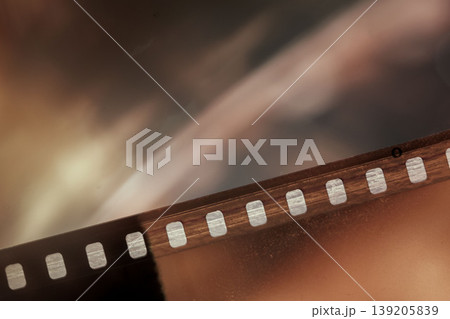 Macro closeup of film strip with sprocket holes, grain, blurred studio background. Concept of film archive, photography, cinema production, memory storage, analog media preservation Macro closeup of film strip with sprocket holes, grain, blurred studio background. Concept of film archive, photography, cinema production, memory storage, analog media preservation 139205839