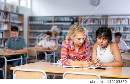 Two teenage friends sit at a desk in school library and carefully do assignments 139205870