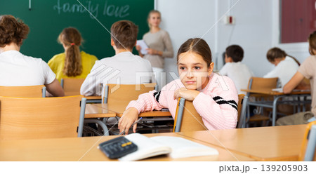 Sad young schoolgirl sitting at desk during lesson 139205903