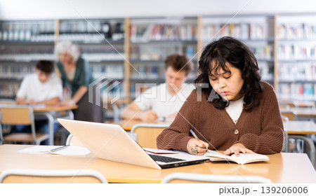 Schoolgirl studies on a laptop and writes notes in a copybook Schoolgirl studies on a laptop and writes notes in a copybook 139206006