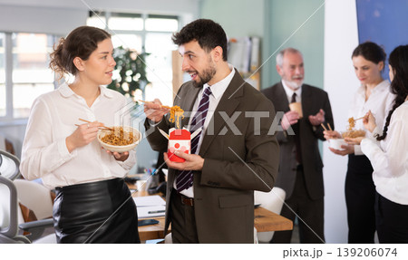 Office workers, man and girl, eating noodles during their break and chatting with each other indoor Office workers, man and girl, eating noodles during their break and chatting with each other indoor 139206074