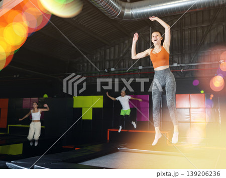 Happy middle aged woman practicing and jumping on trampolines in a sports indoor center, workout and modern entertainment concept Happy middle aged woman practicing and jumping on trampolines in a sports indoor center, workout and modern entertainment concept 139206236