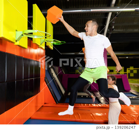 Athletic people throw ball into basketball basket while jumping on trampolines at an entertainment center Athletic people throw ball into basketball basket while jumping on trampolines at an entertainment center 139206247