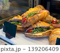 Croissant sandwiches with cheese, salami, and arugula in display case. Bakery assortment, ready food choice, snack purchase, and cafe offering with layered ingredients. 139206409