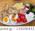 Assorted breakfast plate with eggs, tomato, cheese, ham, salad, radish, cream and grilled bread on a wooden table. Balanced brunch, cafe meal, protein, dairy, vegetable and bakery serving. 139206433