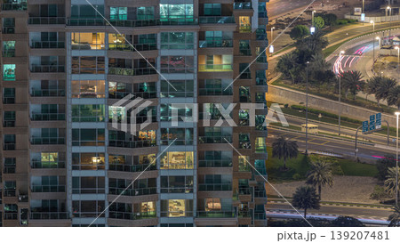 Rows of glowing windows with people in apartment building at night. 139207481