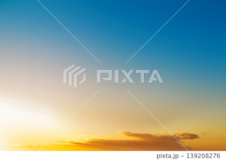 A clear sky featuring a vibrant gradient from deep blue to bright orange during sunset or sunrise, with a few soft clouds on the horizon A clear sky featuring a vibrant gradient from deep blue to bright orange during sunset or sunrise, with a few soft clouds on the horizon 139208276