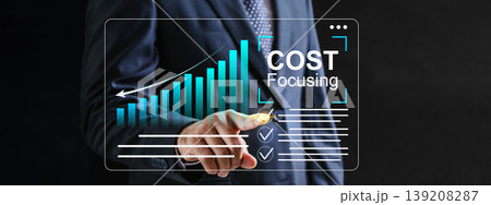Businessman in a suit interacting with a virtual dashboard showing bar charts and cost focusing text, highlighting strategic financial management and efficiency 139208287