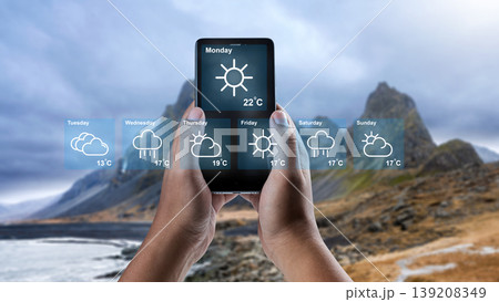 Close-up of hands holding a smartphone with an augmented reality weather forecast overlay, showing a weekly outlook against a blurred mountain background Close-up of hands holding a smartphone with an augmented reality weather forecast overlay, showing a weekly outlook against a blurred mountain background 139208349