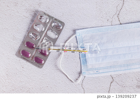 A thermometer, a medical mask, and a blister pack of pills on the table top view A thermometer, a medical mask, and a blister pack of pills on the table top view 139209237