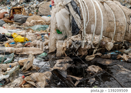 People are working at a waste management site where garbage is piled high. Plastic bags and containers are spread throughout the area People are working at a waste management site where garbage is piled high. Plastic bags and containers are spread throughout the area 139209509