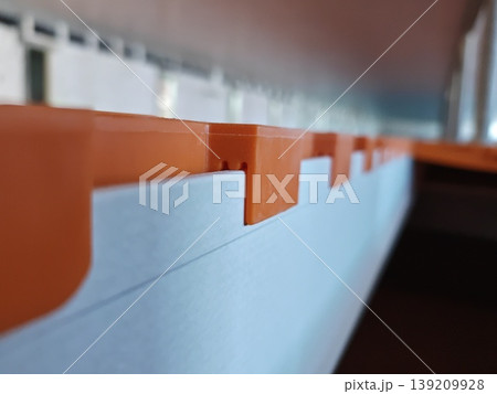 Close up side view of orange plastic slatted flooring panel edge with locking tabs installed on support beam in pig farm. Livestock farming, agriculture equipment, construction 139209928