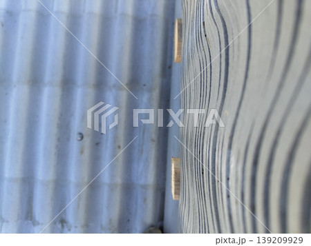 Corrugated fiber cement roofing sheets installed with visible wave profile and mounting on wooden supports in outdoor setting. Roofing, construction, building materials, exterior installation 139209929