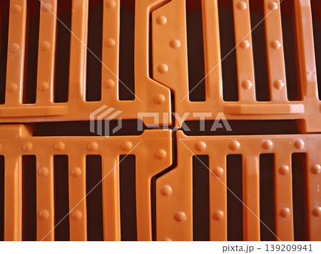 Top view of orange plastic slatted flooring panels with interlocking joints and drainage slots for pig housing system. Livestock farming, agriculture equipment, animal housing Top view of orange plastic slatted flooring panels with interlocking joints and drainage slots for pig housing system. Livestock farming, agriculture equipment, animal housing 139209941