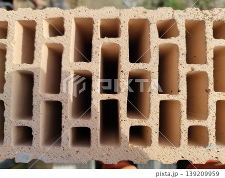 Hollow clay brick with multiple rectangular cavities shown in close up on construction site. Building materials, masonry, construction, architecture, wall building Hollow clay brick with multiple rectangular cavities shown in close up on construction site. Building materials, masonry, construction, architecture, wall building 139209959