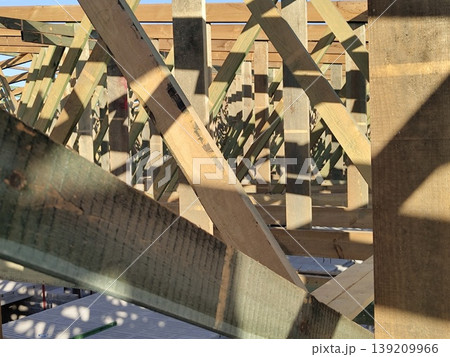 Wooden roof frame structure under construction with intersecting beams and trusses in daylight at building site. Construction, architecture, carpentry, engineering, housing development Wooden roof frame structure under construction with intersecting beams and trusses in daylight at building site. Construction, architecture, carpentry, engineering, housing development 139209966
