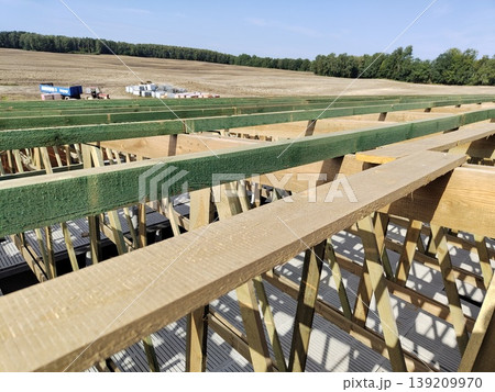 Wooden roof frame under construction with beams and trusses arranged across building structure in rural outdoor area. Construction, carpentry, architecture, housing development, engineering Wooden roof frame under construction with beams and trusses arranged across building structure in rural outdoor area. Construction, carpentry, architecture, housing development, engineering 139209970