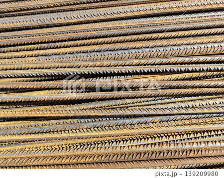 Rusted steel reinforcement bars stacked in dense horizontal layers with ribbed texture and oxidation on construction site. Building materials, metal industry, structural reinforcement 139209980