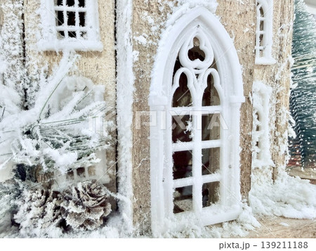 enchanting frosted gothic window on miniature winter cottage with pine cone accents and snowdrifts for seasonal wallpaper or holiday banner background enchanting frosted gothic window on miniature winter cottage with pine cone accents and snowdrifts for seasonal wallpaper or holiday banner background 139211188