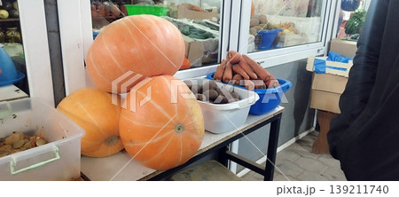 Vibrant display of autumn harvest vegetables sits on a market stall. Three large, pale orange pumpkins are stacked beside plastic bins filled with fresh carrots and dark beets, ready for sale Vibrant display of autumn harvest vegetables sits on a market stall. Three large, pale orange pumpkins are stacked beside plastic bins filled with fresh carrots and dark beets, ready for sale 139211740
