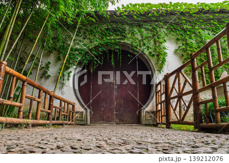 Ornate moon gate leading into a serene classical garden in Suzhou, adorned with lush bamboo and vibrant vines 139212076