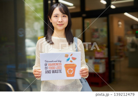 スーパーマーケットの前で食品ロスのプラカードを持つ若い女性 スーパーマーケットの前で食品ロスのプラカードを持つ若い女性 139212479