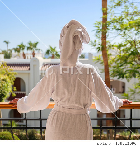A female tourist on the balcony of her hotel room, wearing a white robe and a towel on her head 139212996
