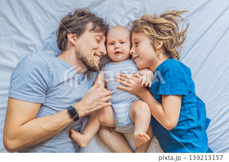 Father lying on bed with two sons, newborn baby and older child at home. Loving dad spending time with kids, bonding and relaxing. Fatherhood, sibling connection and warm family life concept Father lying on bed with two sons, newborn baby and older child at home. Loving dad spending time with kids, bonding and relaxing. Fatherhood, sibling connection and warm family life concept 139213157