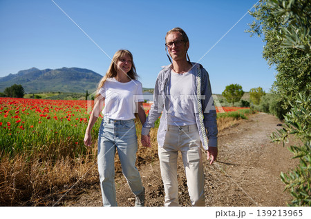 Couple Walking Hand in Hand Through Poppy Field Near Mountains on Sunny Day Couple Walking Hand in Hand Through Poppy Field Near Mountains on Sunny Day 139213965