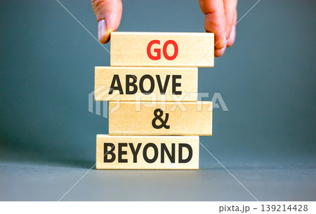 Go above and beyond symbol. Concept words Go above and beyond on beautiful wooden blocks. Beautiful grey background. Businessman hand. Business motivational Go above and beyond concept. Copy space. Go above and beyond symbol. Concept words Go above and beyond on beautiful wooden blocks. Beautiful grey background. Businessman hand. Business motivational Go above and beyond concept. Copy space. 139214428