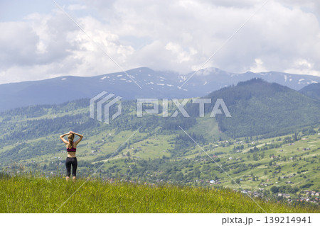 Slim young woman with raised arms outdoors on background of beautiful mountain landscape on sunny summer day. Slim young woman with raised arms outdoors on background of beautiful mountain landscape on sunny summer day. 139214941