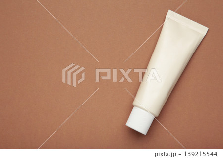 Beige tube of cream on brown background. Mockup plastic tube for cosmetics. Space for text Beige tube of cream on brown background. Mockup plastic tube for cosmetics. Space for text 139215544