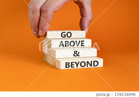 Go above and beyond symbol. Concept words Go above and beyond on beautiful wooden blocks. Beautiful orange background. Businessman hand. Business motivational Go above and beyond concept. Copy space. Go above and beyond symbol. Concept words Go above and beyond on beautiful wooden blocks. Beautiful orange background. Businessman hand. Business motivational Go above and beyond concept. Copy space. 139216040