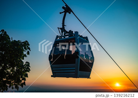 Cable car gondola silhouette against dramatic vivid orange sunset with sun on horizon 139216212