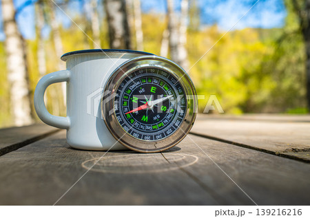 White enamel mug and magnetic compass on wooden table 139216216